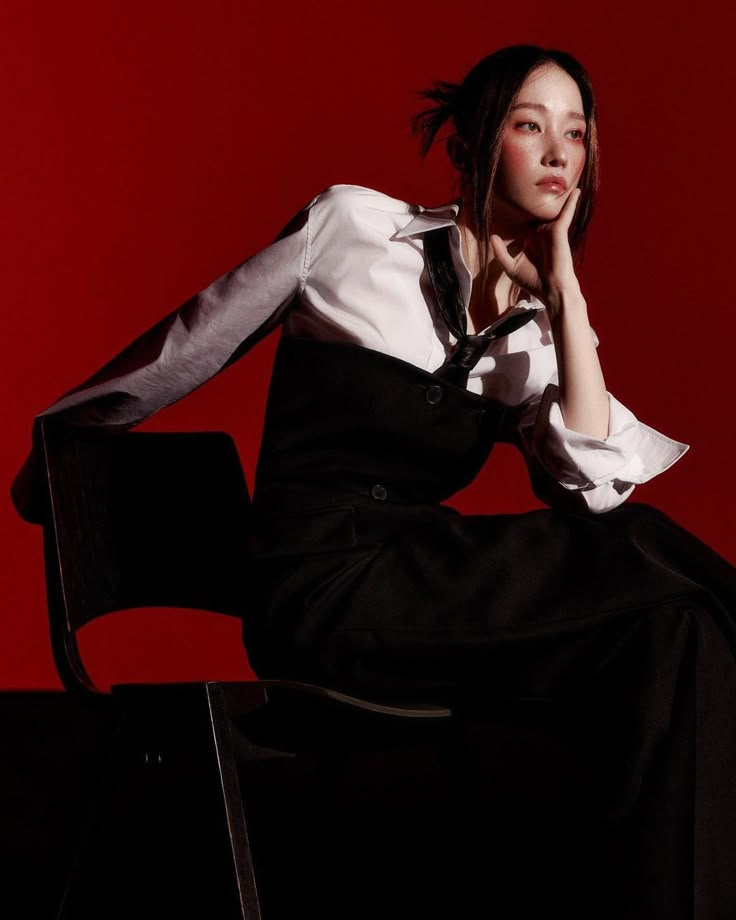 a woman sitting on top of a chair in front of a red wall with her hand under her chin