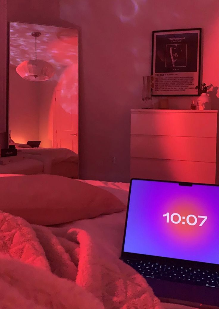 a laptop computer sitting on top of a bed in a room with red lights and pink lighting