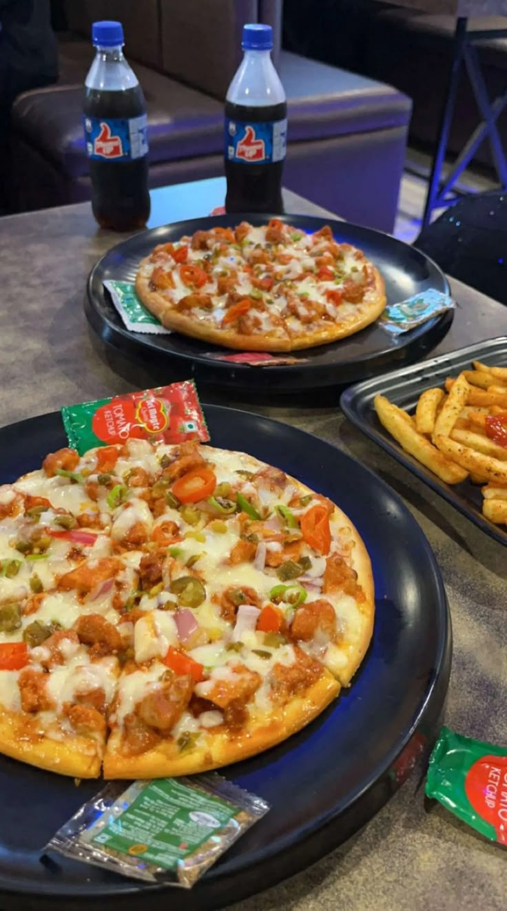 two pizzas sitting on top of black plates next to french fries and water bottles