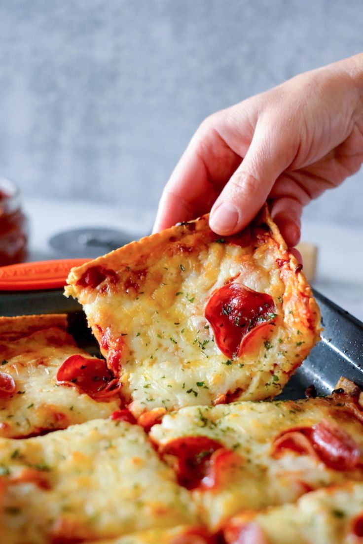 a person taking a slice of pizza from a pan with other food items in the background