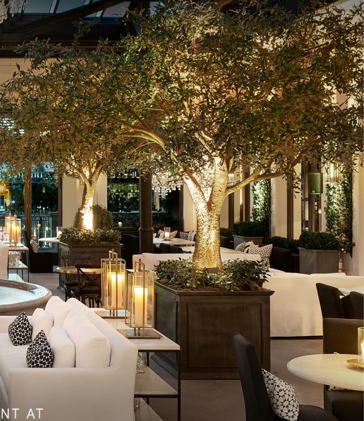 the interior of a restaurant with tables, chairs and candles lit up in front of trees