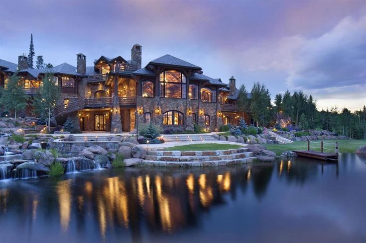 a large house sitting on top of a lush green hillside next to a lake at night