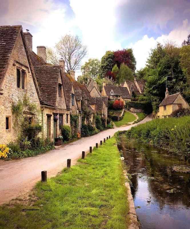 a row of houses next to a river in the middle of a lush green field