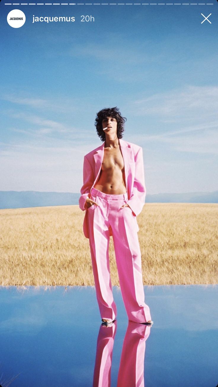 a man in a pink suit standing on the edge of a body of water with his shirt off