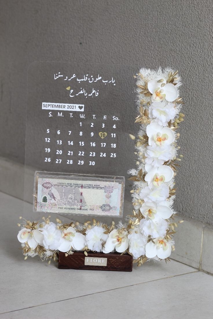 a desk calendar with flowers on it next to a glass frame that reads the date in arabic