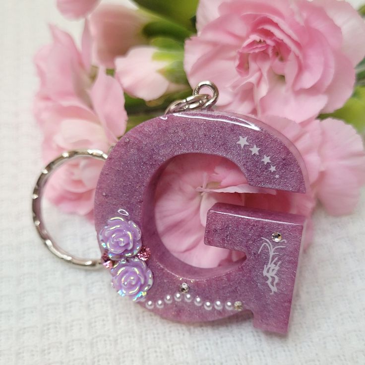 the letter g is made out of purple glitter and has flowers around it on a white tablecloth