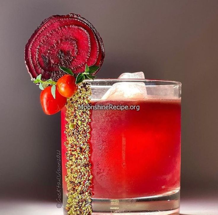 a red drink in a glass with a garnish on the rim next to a slice of tomato