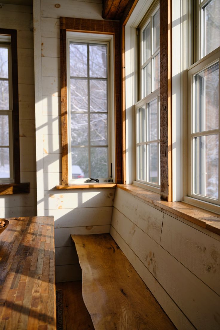 a wooden bench sitting next to two windows in a room with white walls and wood flooring