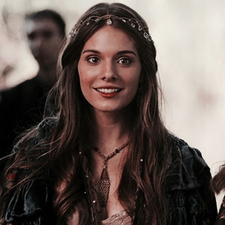 a woman with long brown hair wearing a headpiece and smiling at the camera while standing in front of other people