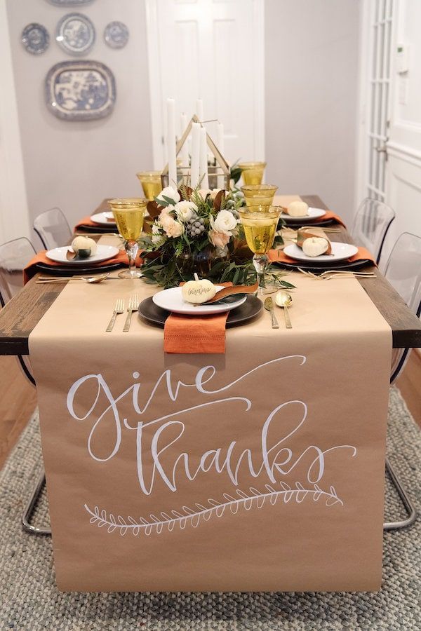 a table set for thanksgiving dinner with place settings and napkins on it, along with an orange ribbon that says give thanks