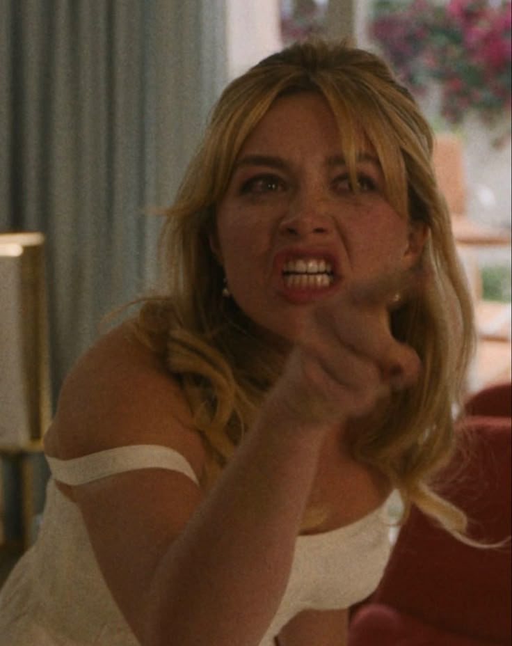 a woman in a white dress brushing her teeth and looking at the camera while sitting on a red couch