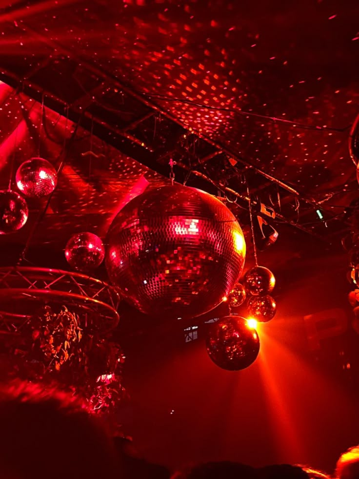 disco balls hanging from the ceiling in a club with red lights and people watching them