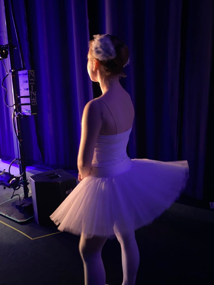 a woman in a white tutu standing next to a purple stage curtain and microphone