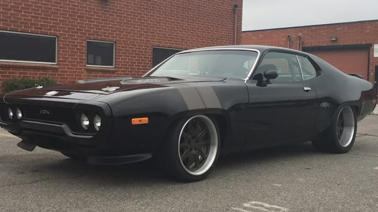 a black muscle car parked in front of a brick building with white rims on it's tires