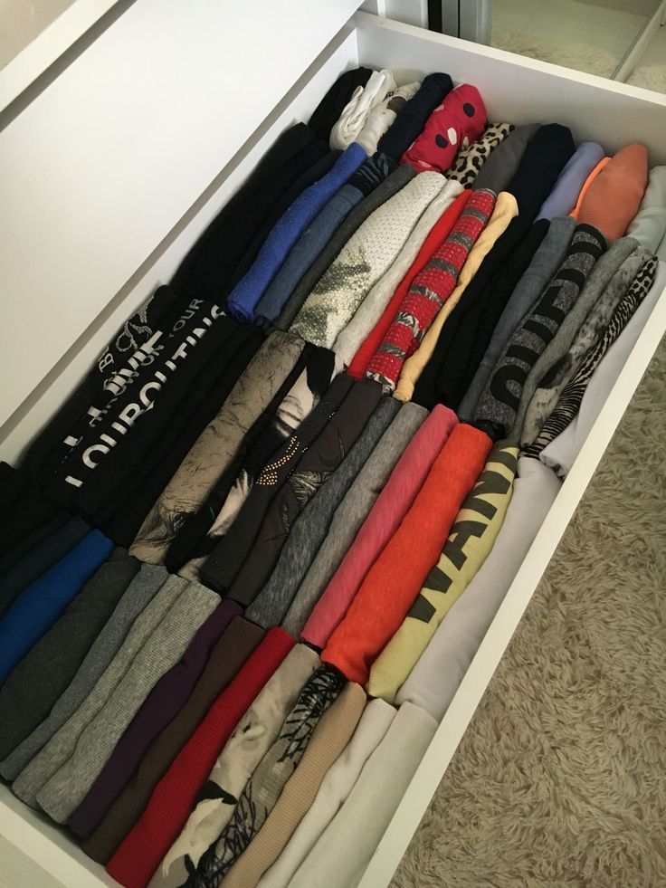 an open drawer filled with lots of different types of shirts and pants on top of carpeted flooring