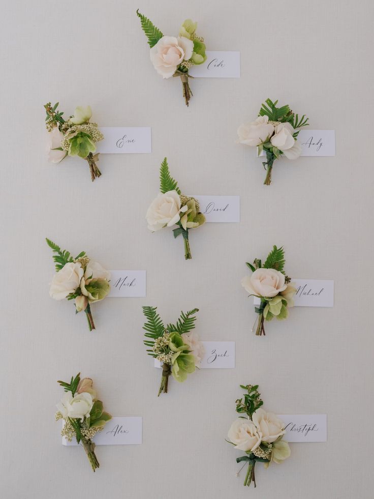 wedding boutonnieres with flowers and greenery laid out on a wall