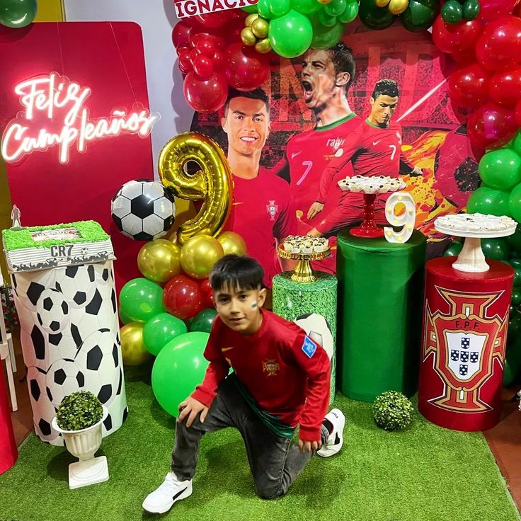 a young boy is posing in front of balloons and decorations for a soccer themed birthday party