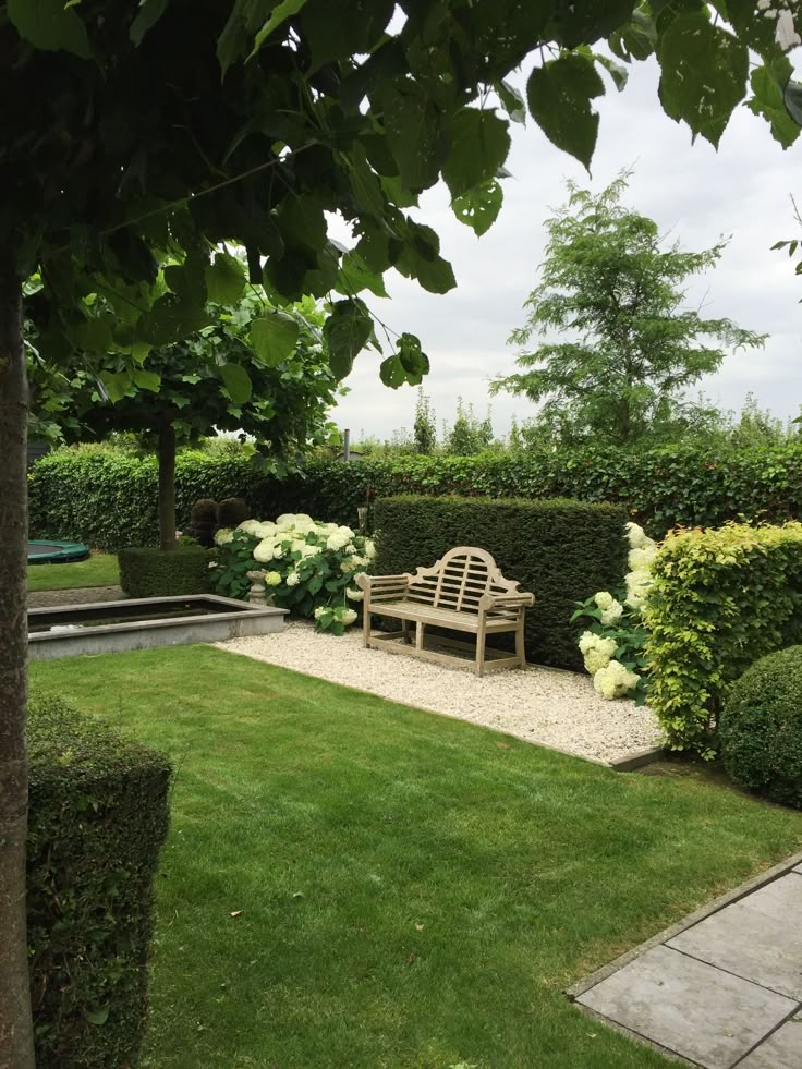 a wooden bench sitting in the middle of a lush green park area with trees and bushes