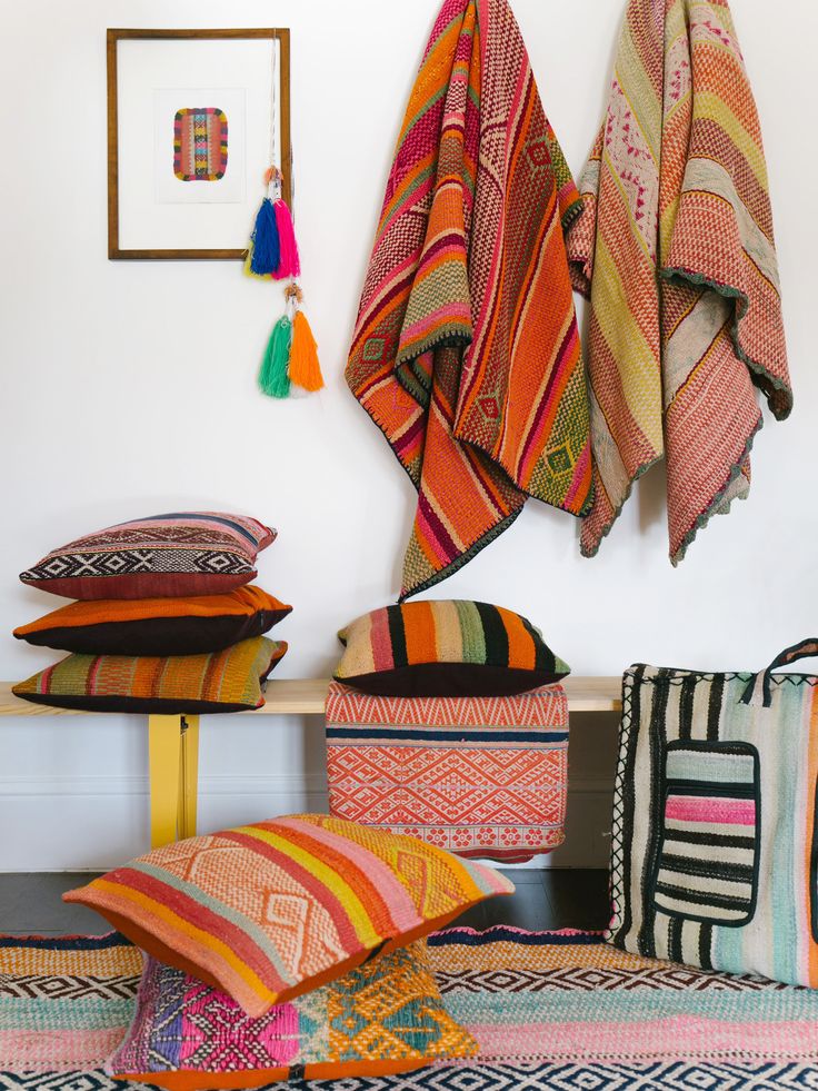 colorful pillows and blankets on a bench in a room with pictures hanging on the wall