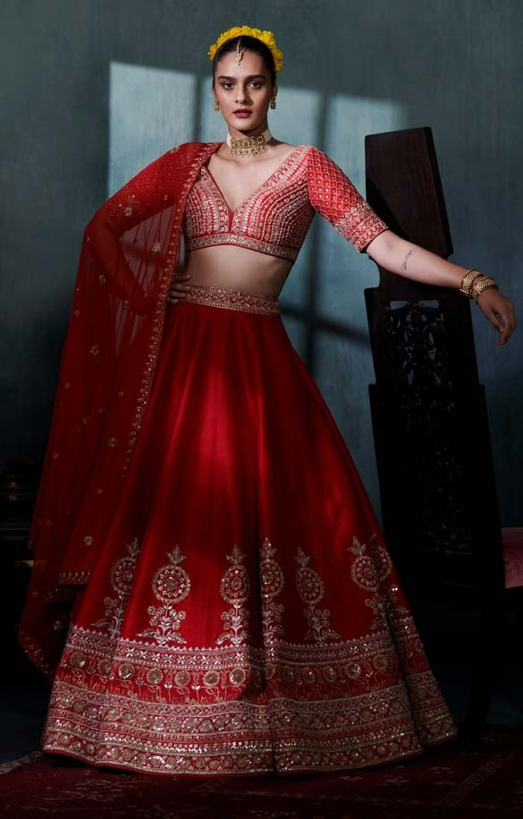 a woman in a red and gold lehenga is posing for the camera with her hands on her hips