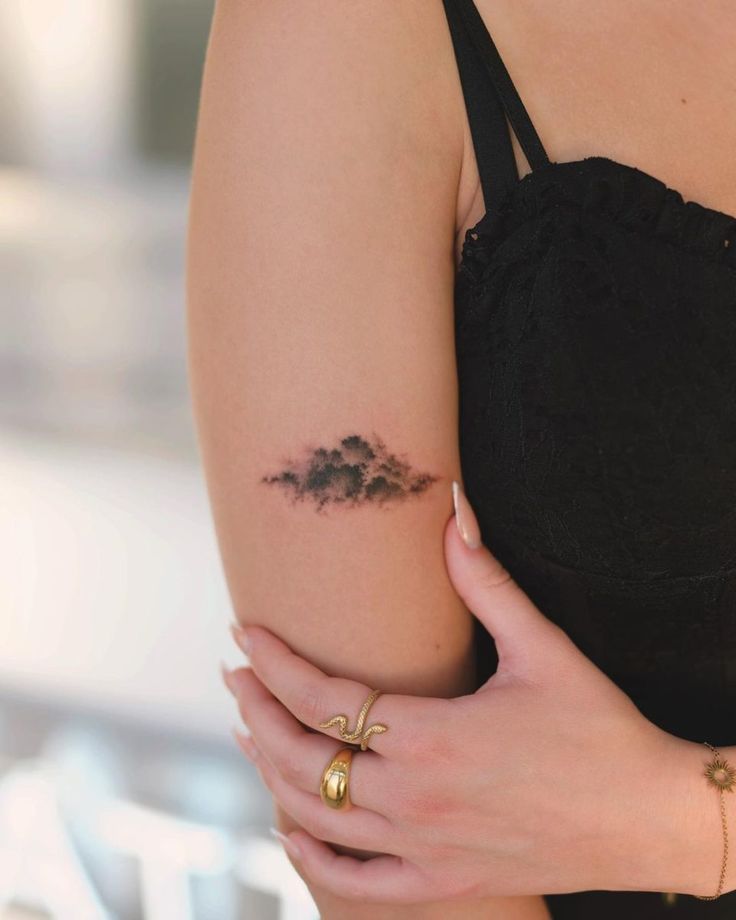 a woman's arm with a small cloud tattoo on it