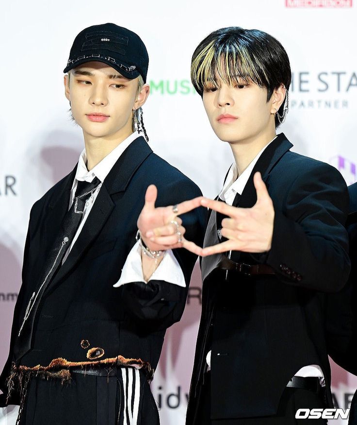 two young men standing next to each other in front of a red carpet and white wall