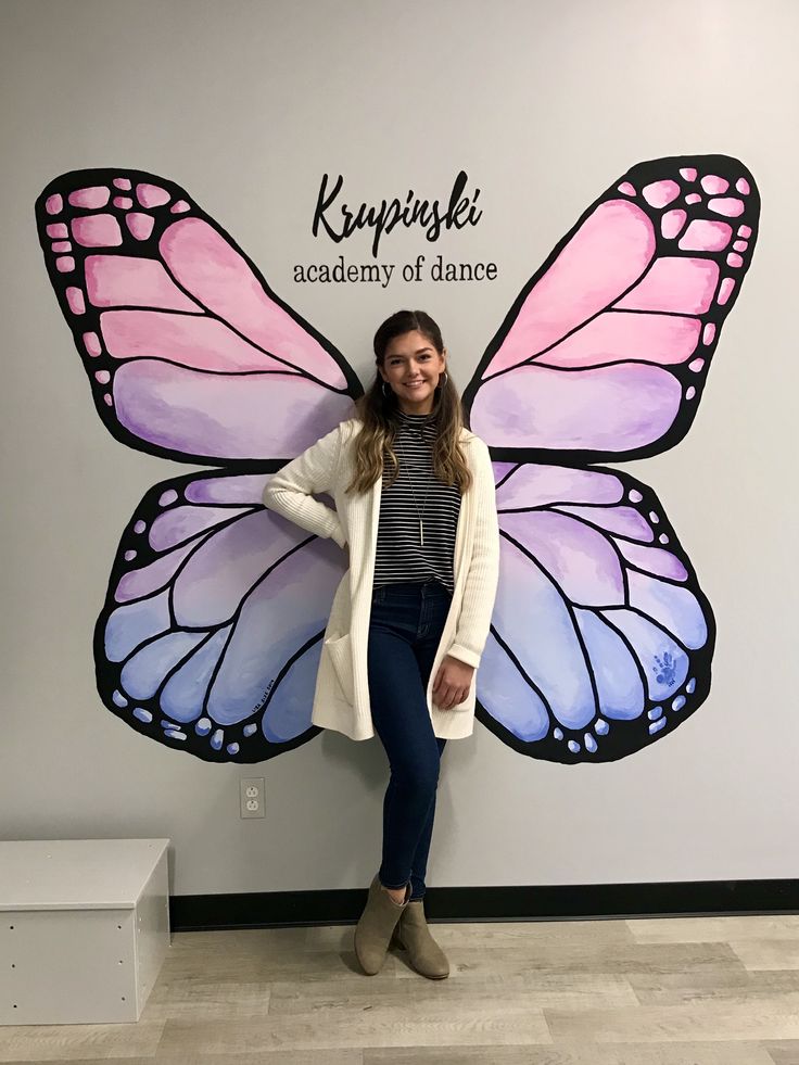 a woman standing in front of a wall with a butterfly painted on it's side