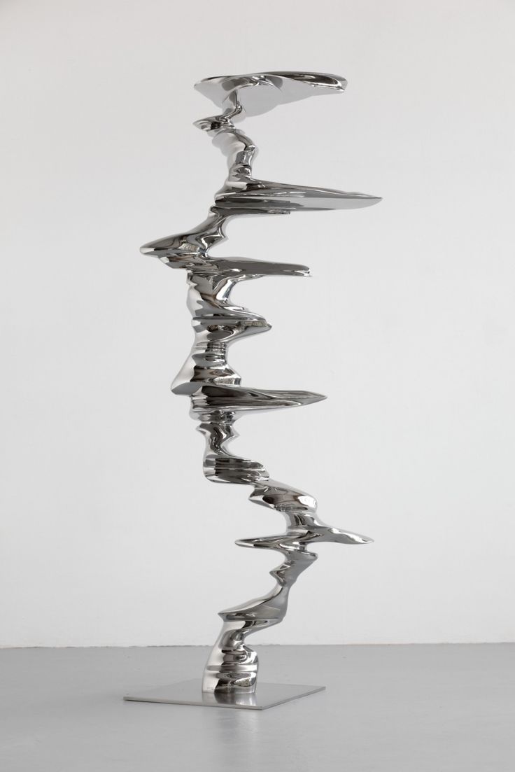 a metal sculpture sitting on top of a white table next to a gray wall and floor