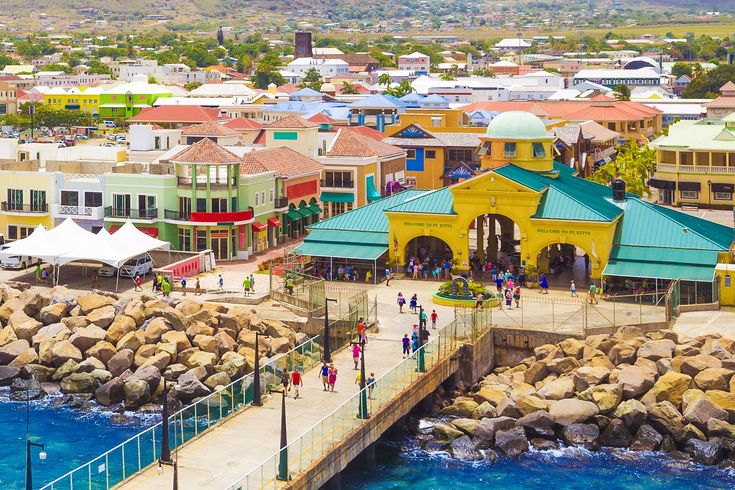 people are walking on the pier in front of some colorful buildings and blue ocean water