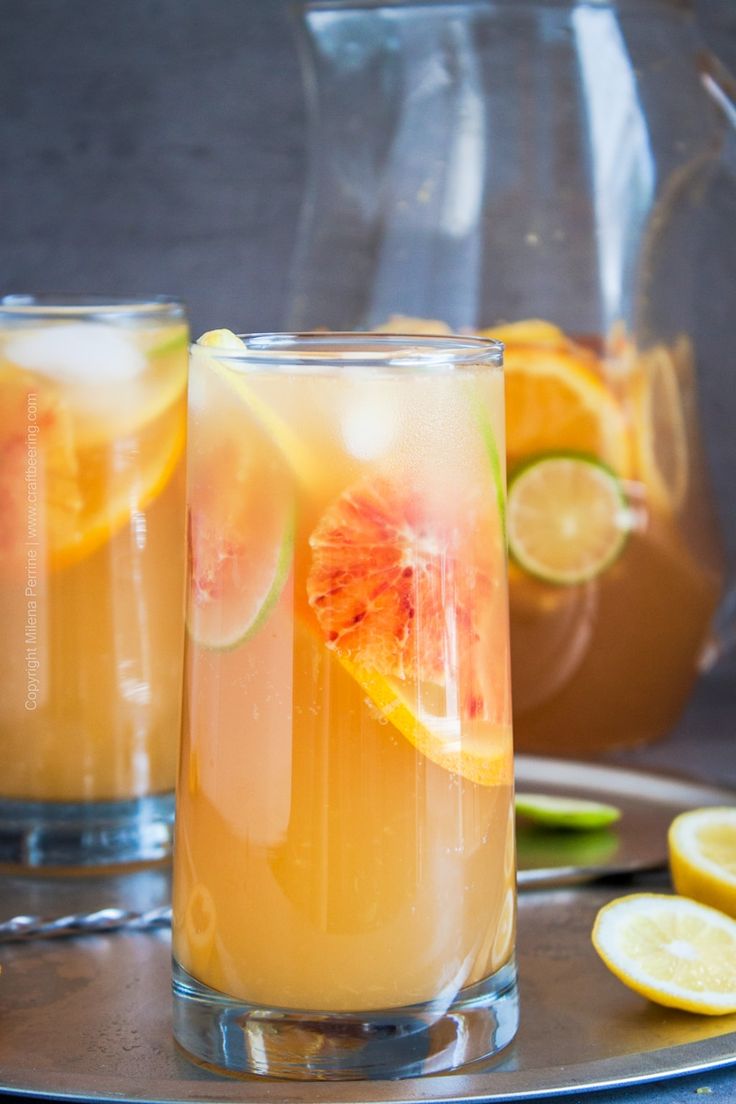 two glasses filled with lemonade and orange slices on a tray next to pitcher of water