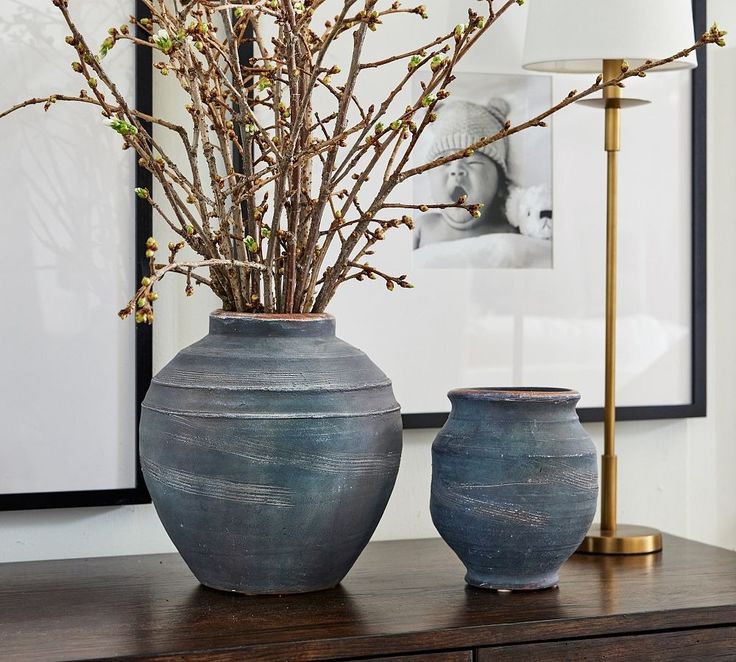 two vases sitting on top of a wooden table next to a lamp and pictures