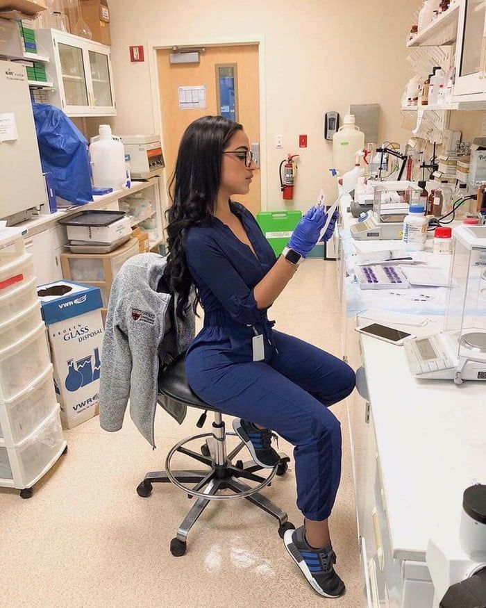 a woman sitting on a chair in a lab holding something up to her face while wearing gloves