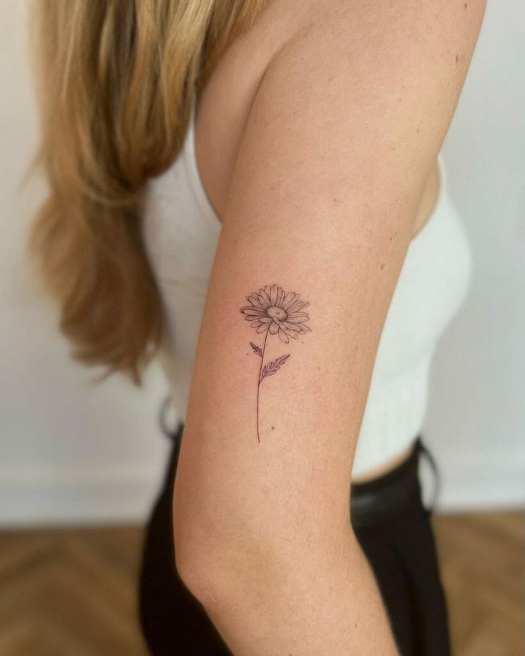 a woman's arm with a small flower tattoo on the back of her left arm