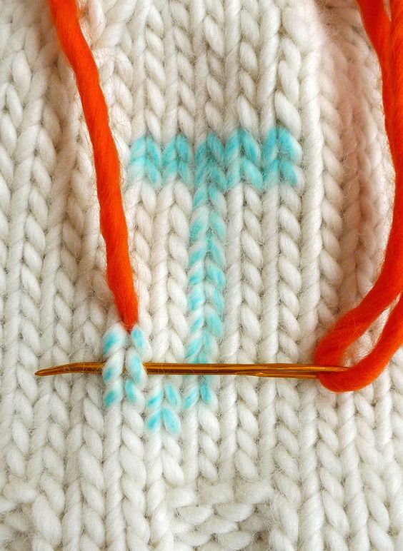 an orange and white knitted object with blue letters on it, next to a knitting needle