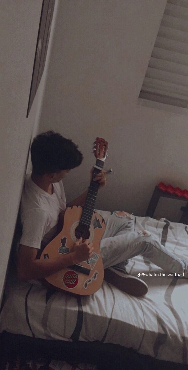 a person sitting on a bed with a guitar in their hand and playing the guitar