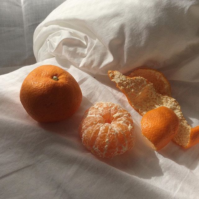 three oranges are sitting on a white sheet and one is half peeled, the other half eaten