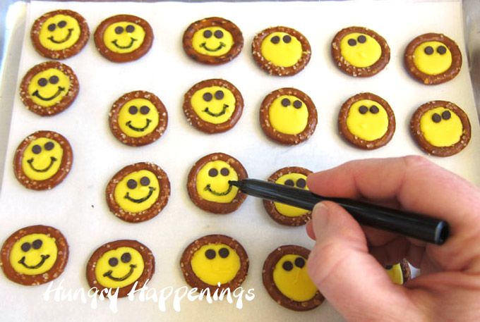 a person holding a marker in front of some cupcakes with smiley faces on them