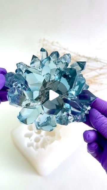 two hands are holding a piece of blue crystal in front of a white object with purple gloves on it