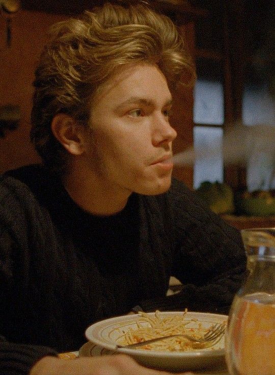 a young man sitting at a table with a plate of food in front of him