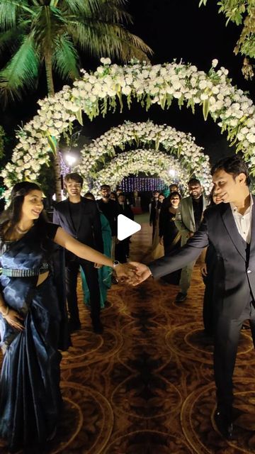 a man and woman shaking hands in front of an archway with white flowers on it