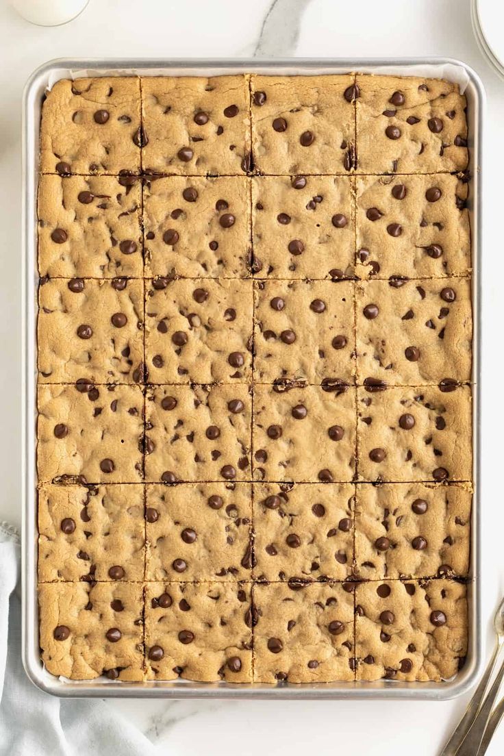 a pan filled with chocolate chip cookie bars on top of a white table next to silverware