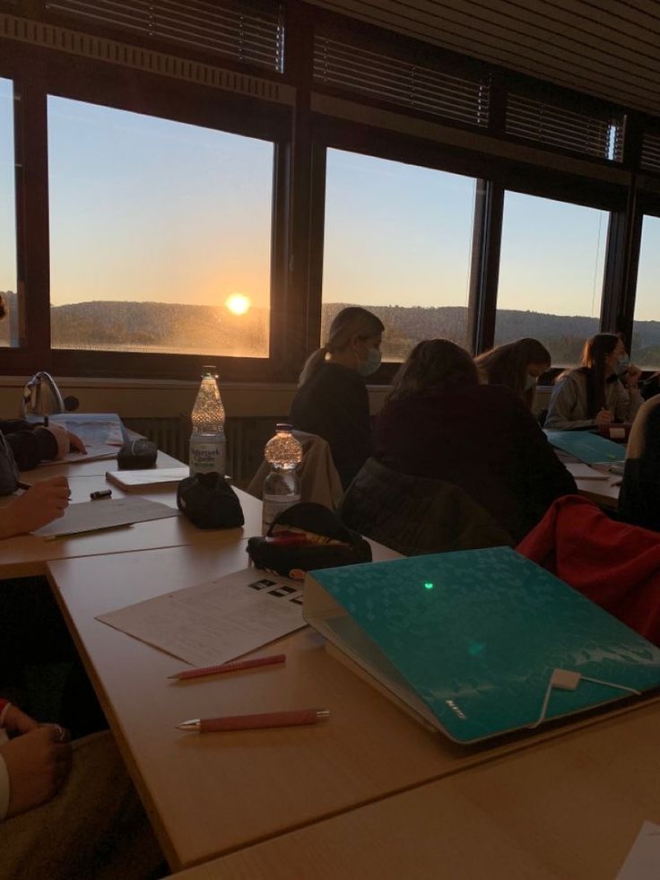 people sitting at tables with laptops and papers in front of large windows looking out onto the ocean