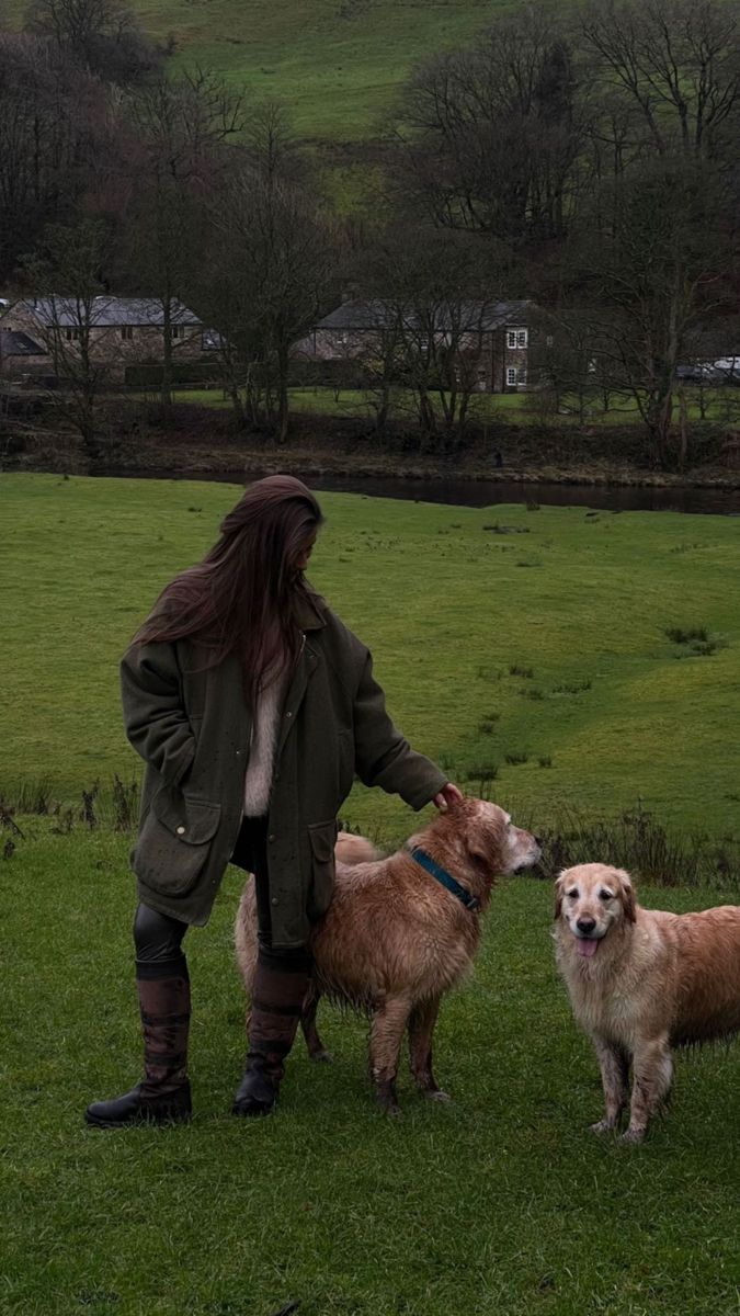 a woman standing next to two dogs on top of a lush green field