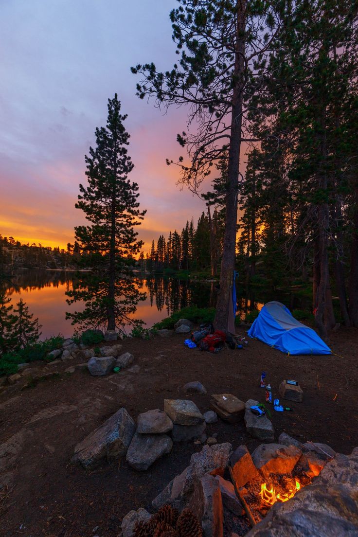 a tent is set up on the shore of a lake at sunset