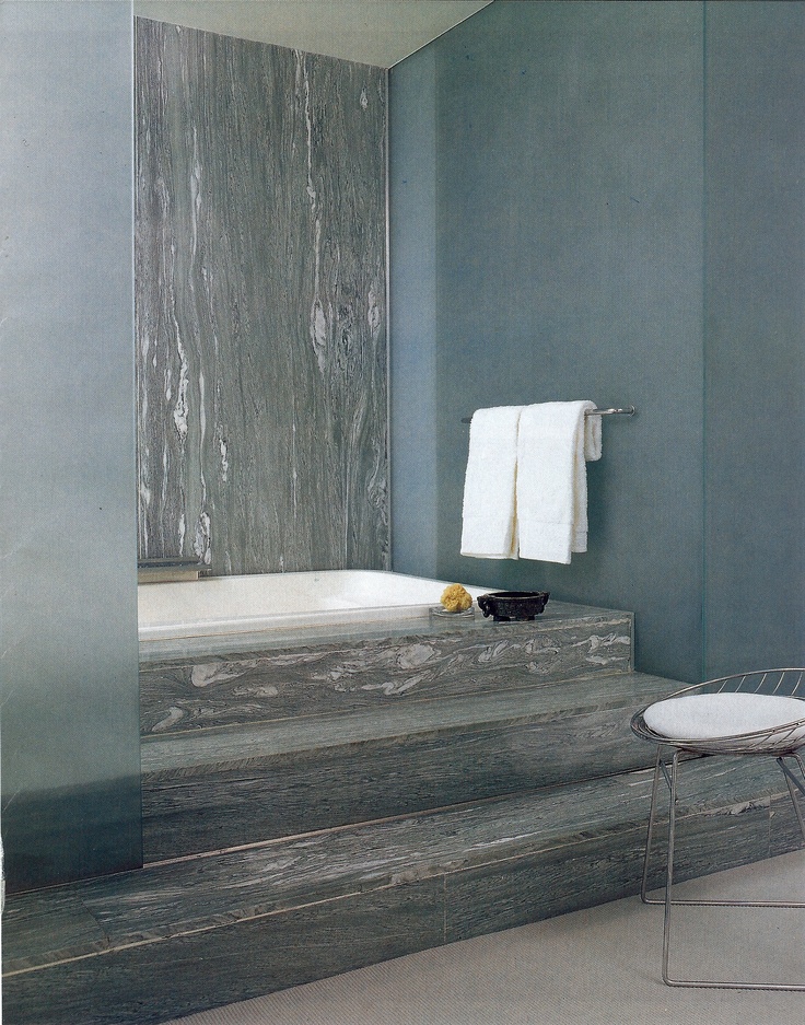 a white chair sitting next to a bath tub in a bathroom with blue walls and flooring