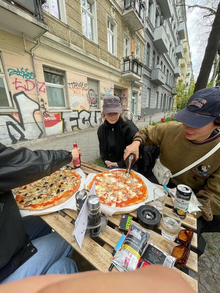 three people sitting at an outdoor table eating pizza