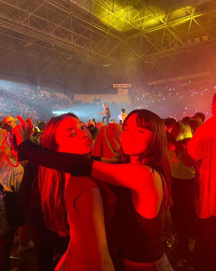 two young women hugging each other in front of an audience at a concert with red lights