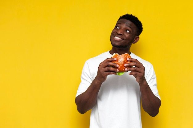 a young man holding up a sandwich in front of his face against a yellow background