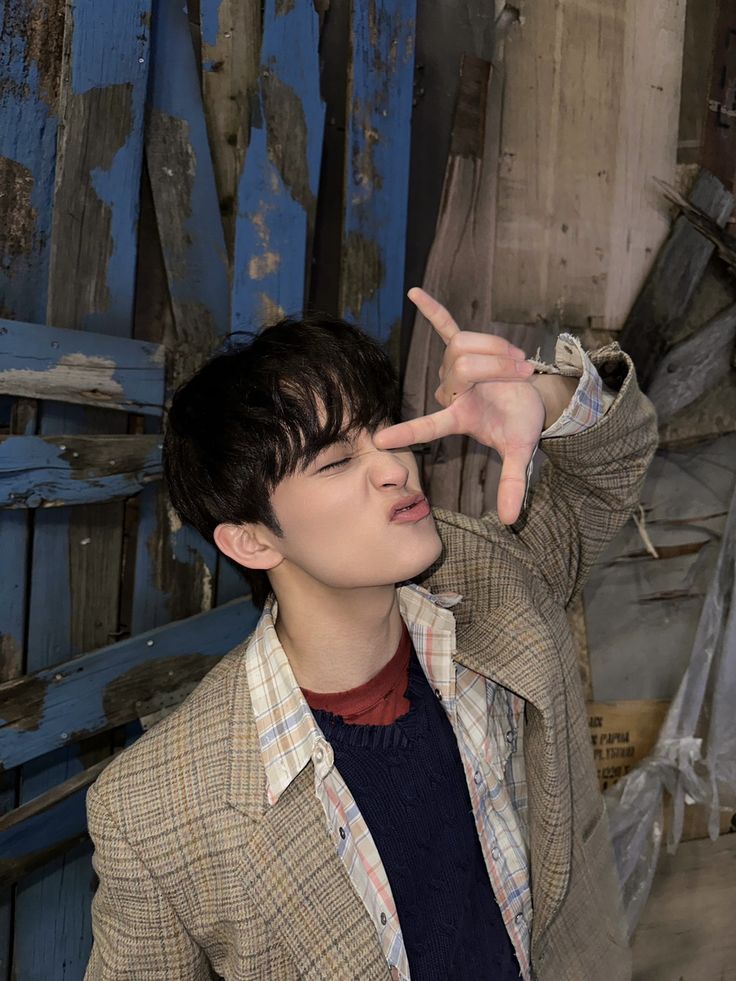 a young man making the peace sign with his hand while standing in front of a wooden wall