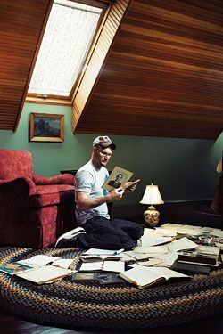 a man sitting on the floor reading a book in front of a red chair and lamp